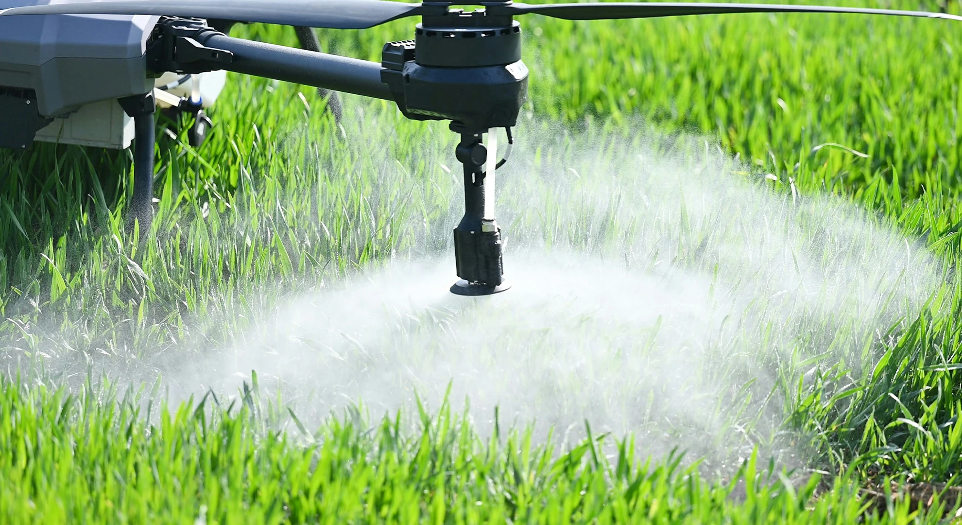 Close-up of an agricultural drone nozzle spraying a fine mist over a green crop field.