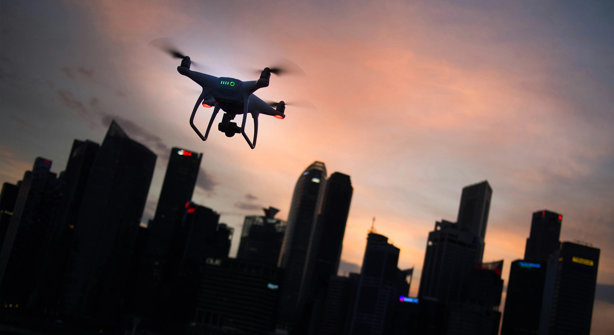 Commercial quadcopter drone flying over a city skyline at sunset during an aerial inspection flight