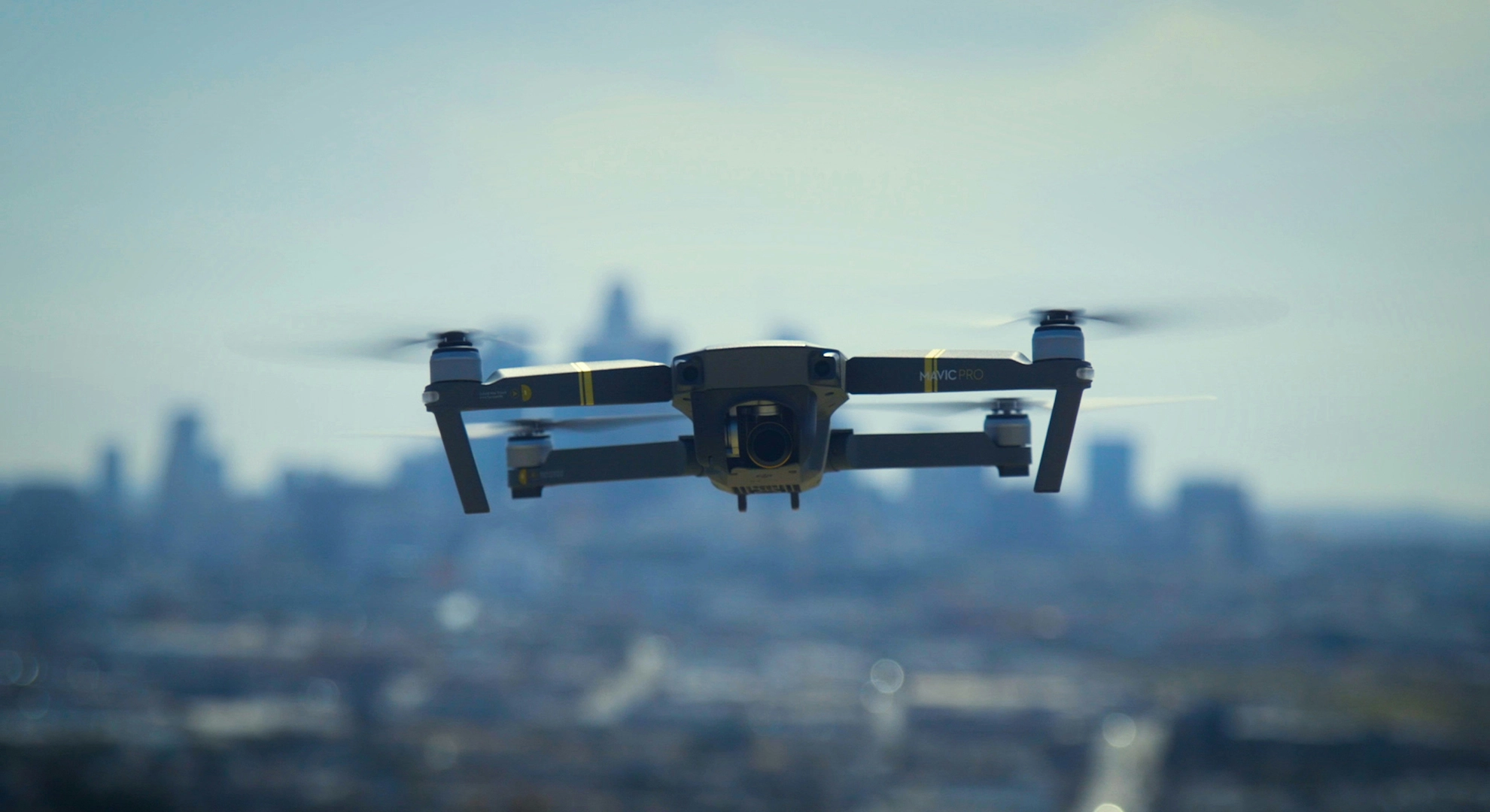 Commercial quadcopter drone hovering in flight over a city skyline during an aerial inspection.