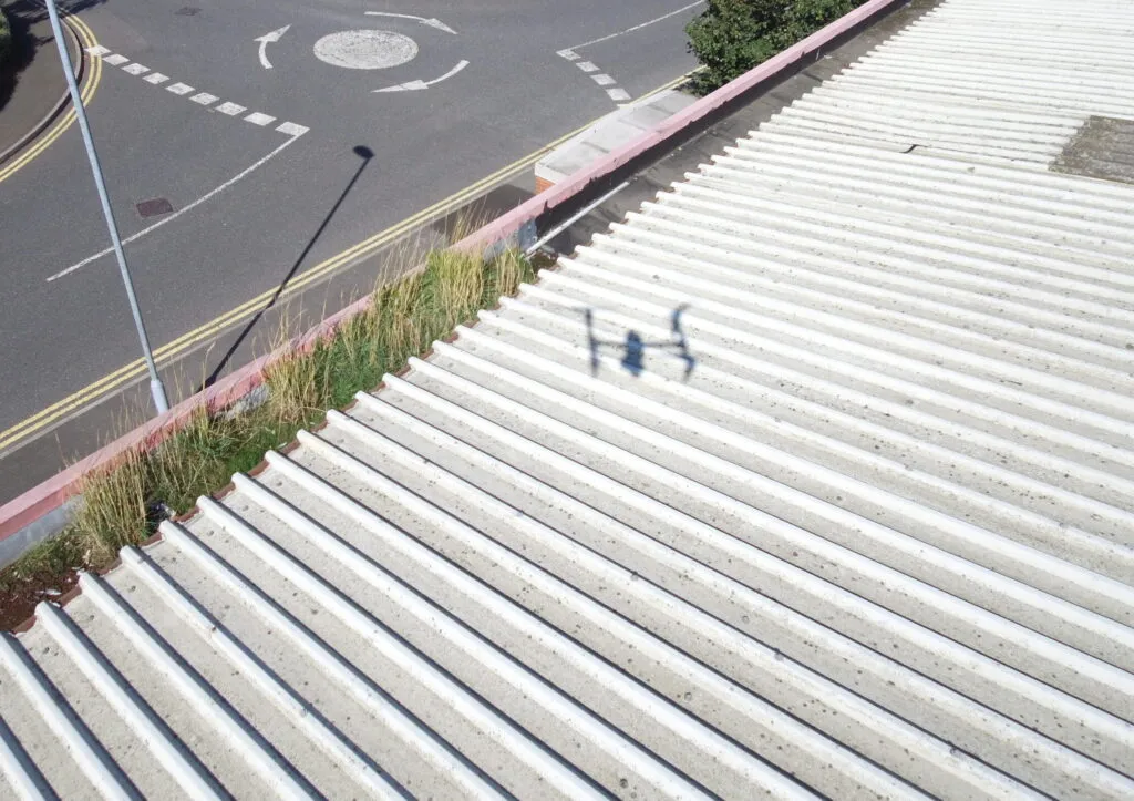 Aerial drone inspection view looking down at a corrugated metal roof with a drone shadow cast on the surface.
