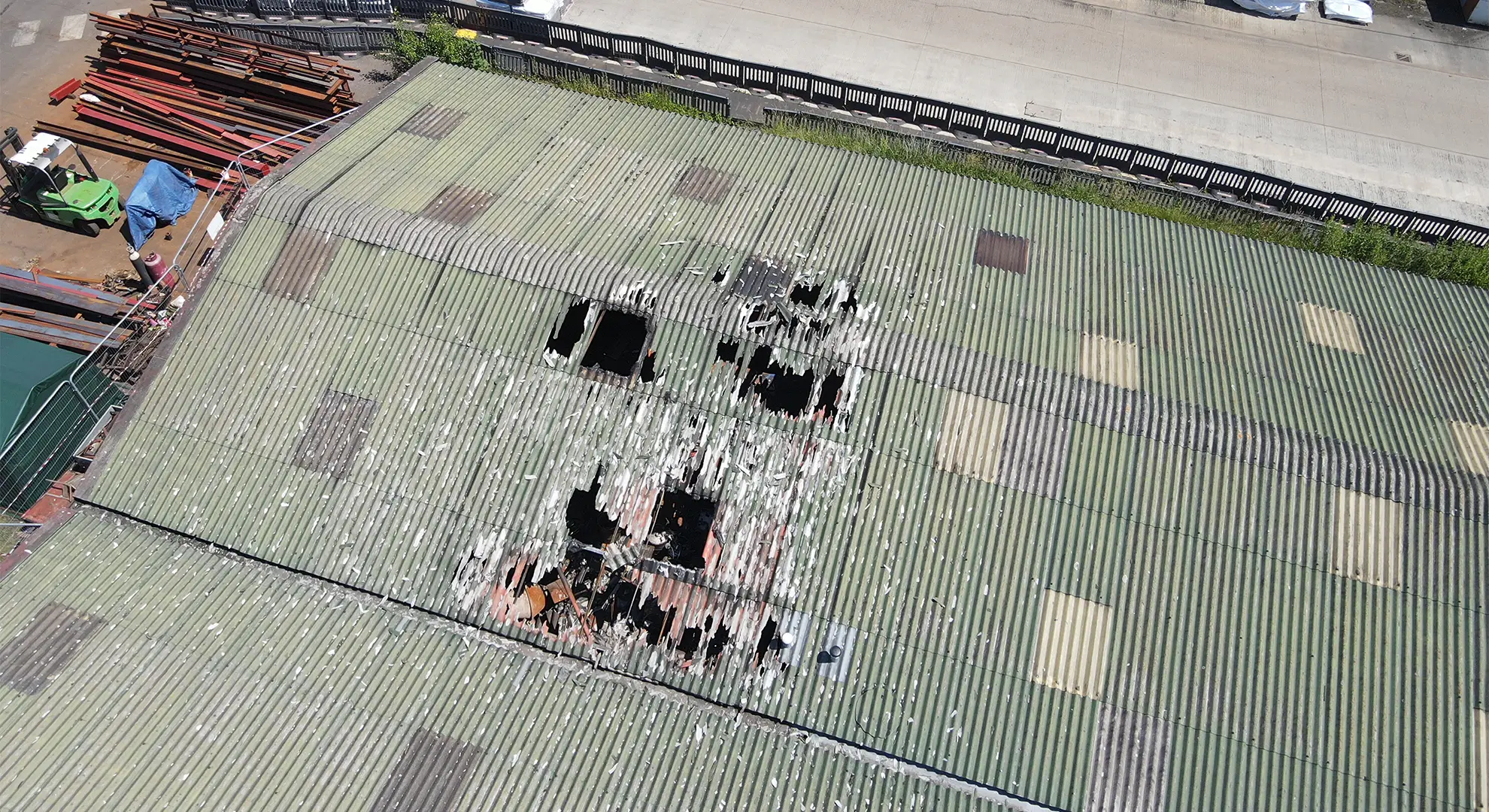 Aerial drone view of significant damage and large holes in a green corrugated metal warehouse roof
