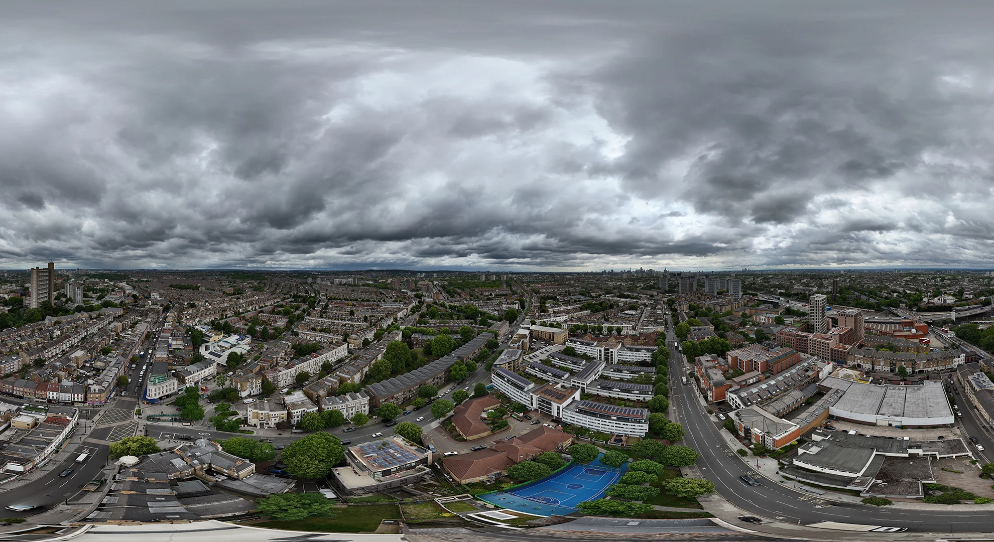 Panoramic drone aerial view of an urban neighbourhood under a dark, dramatic, and cloudy sky