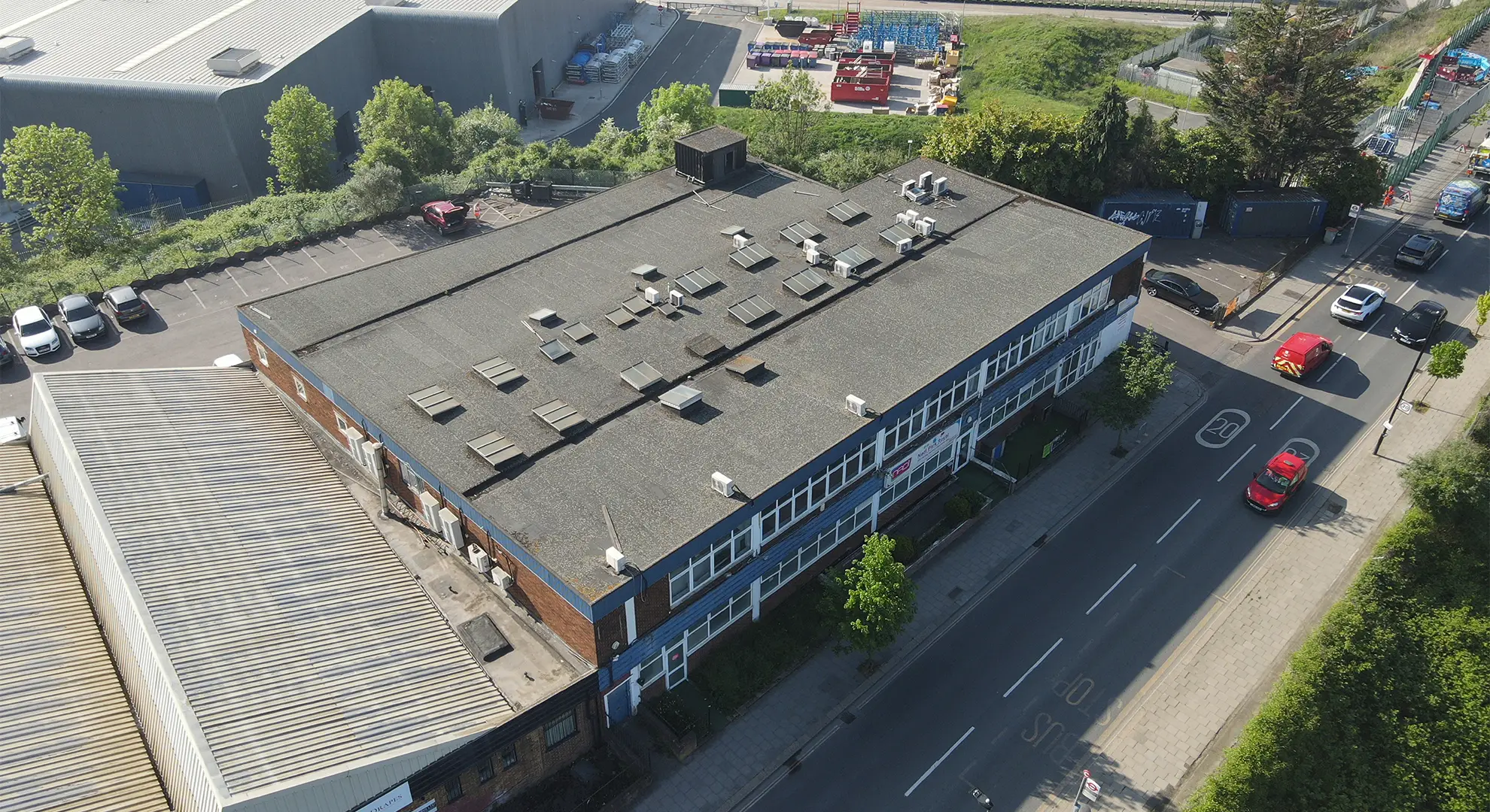 Drone aerial view of a two-story commercial building with a flat roof and skylights, situated on a street corner