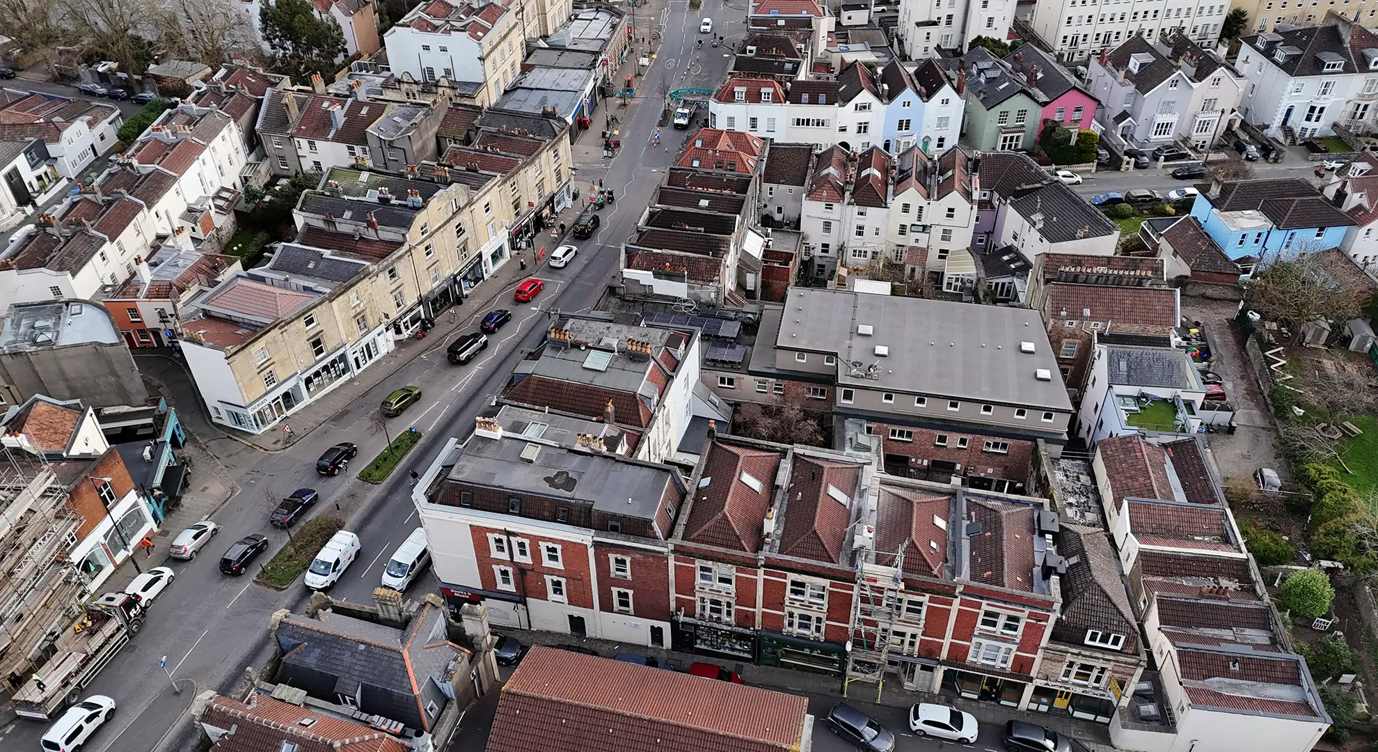 Aerial drone view of a city street with traffic, surrounded by multi-story buildings and a row of colourful houses