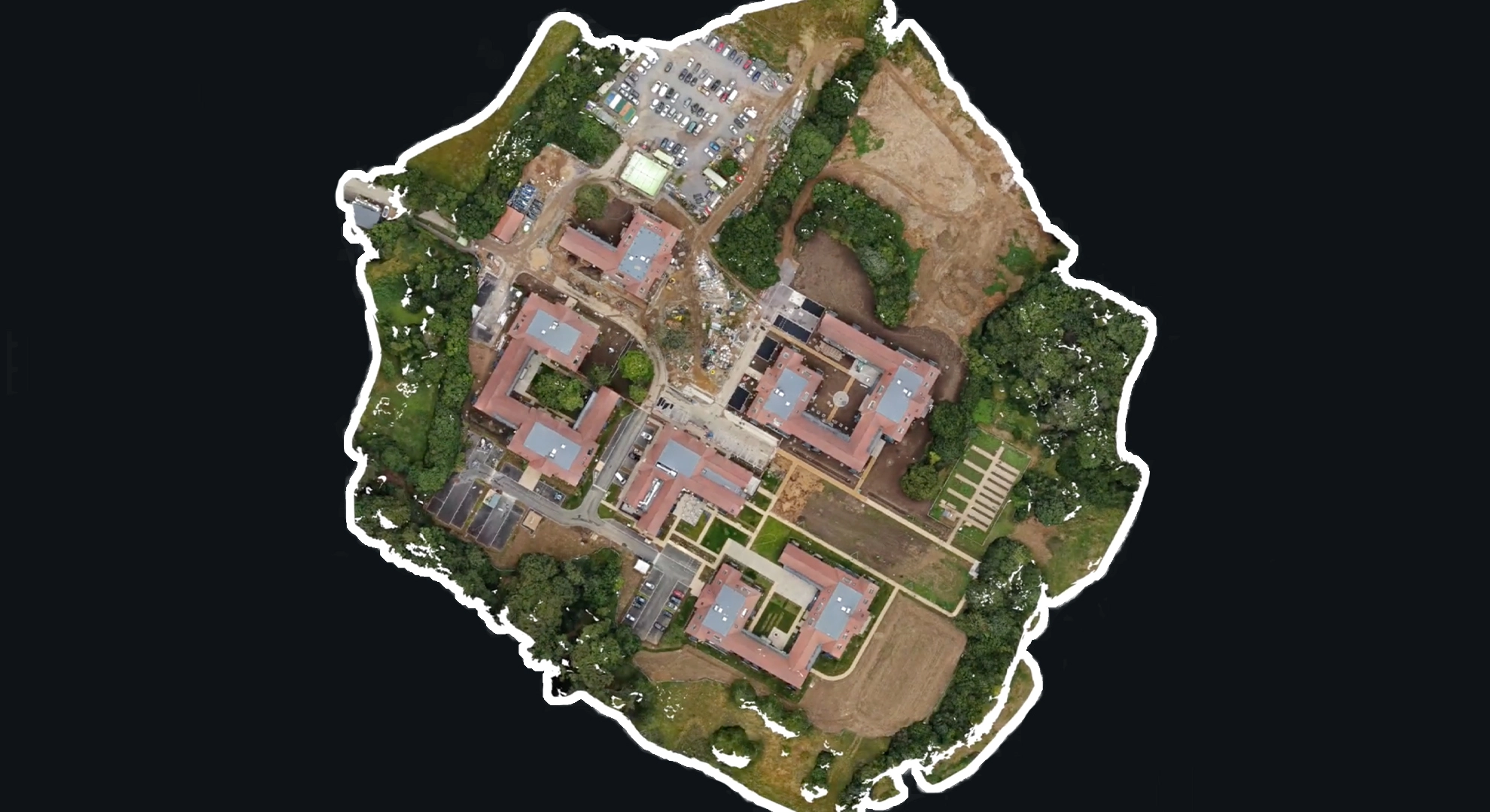 Aerial view of a building complex with red roofs, parking lots, and green spaces