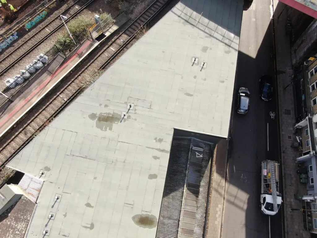 Top-down aerial drone view inspecting a commercial flat roof showing standing water, adjacent to railway tracks and a street.