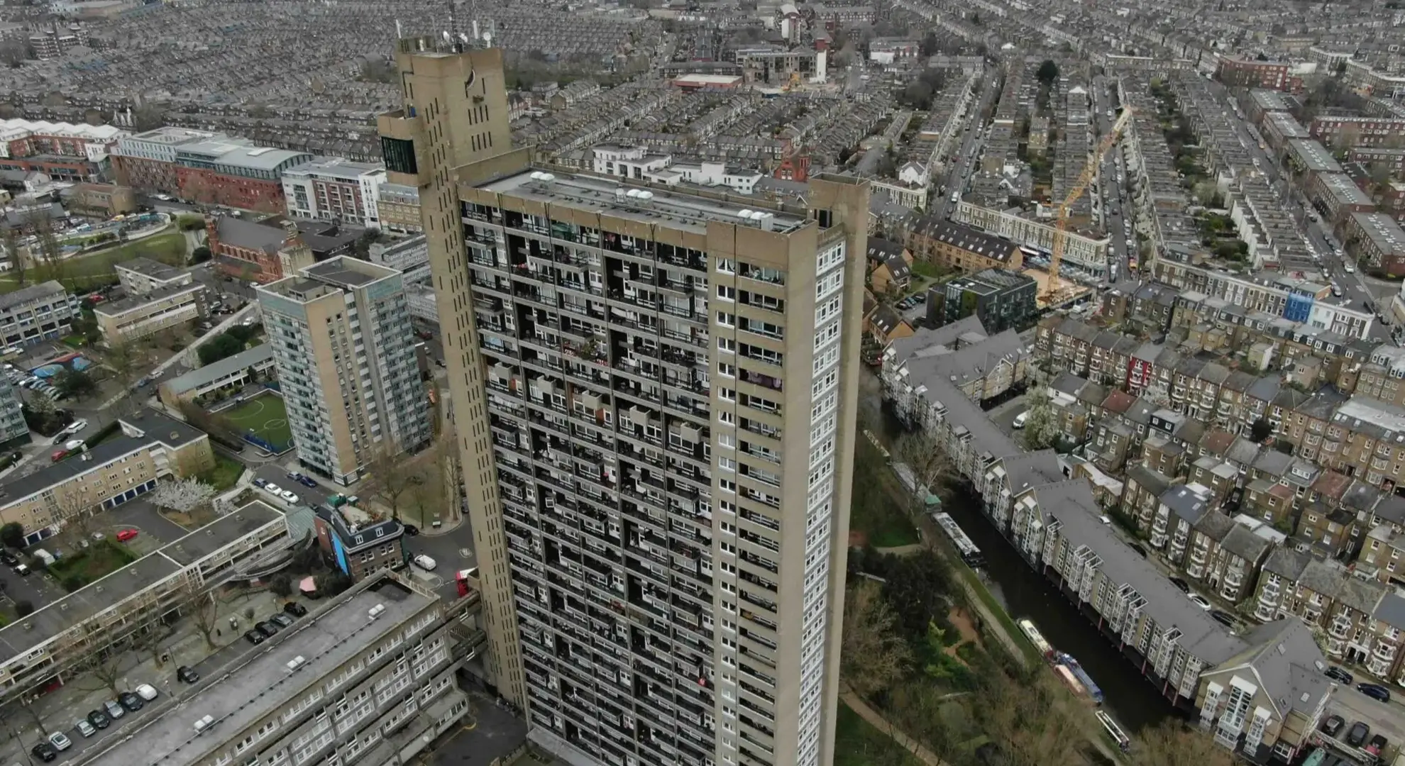 Aerial view of Trellick Tower - a tall brutalist concrete apartment building in a dense urban area