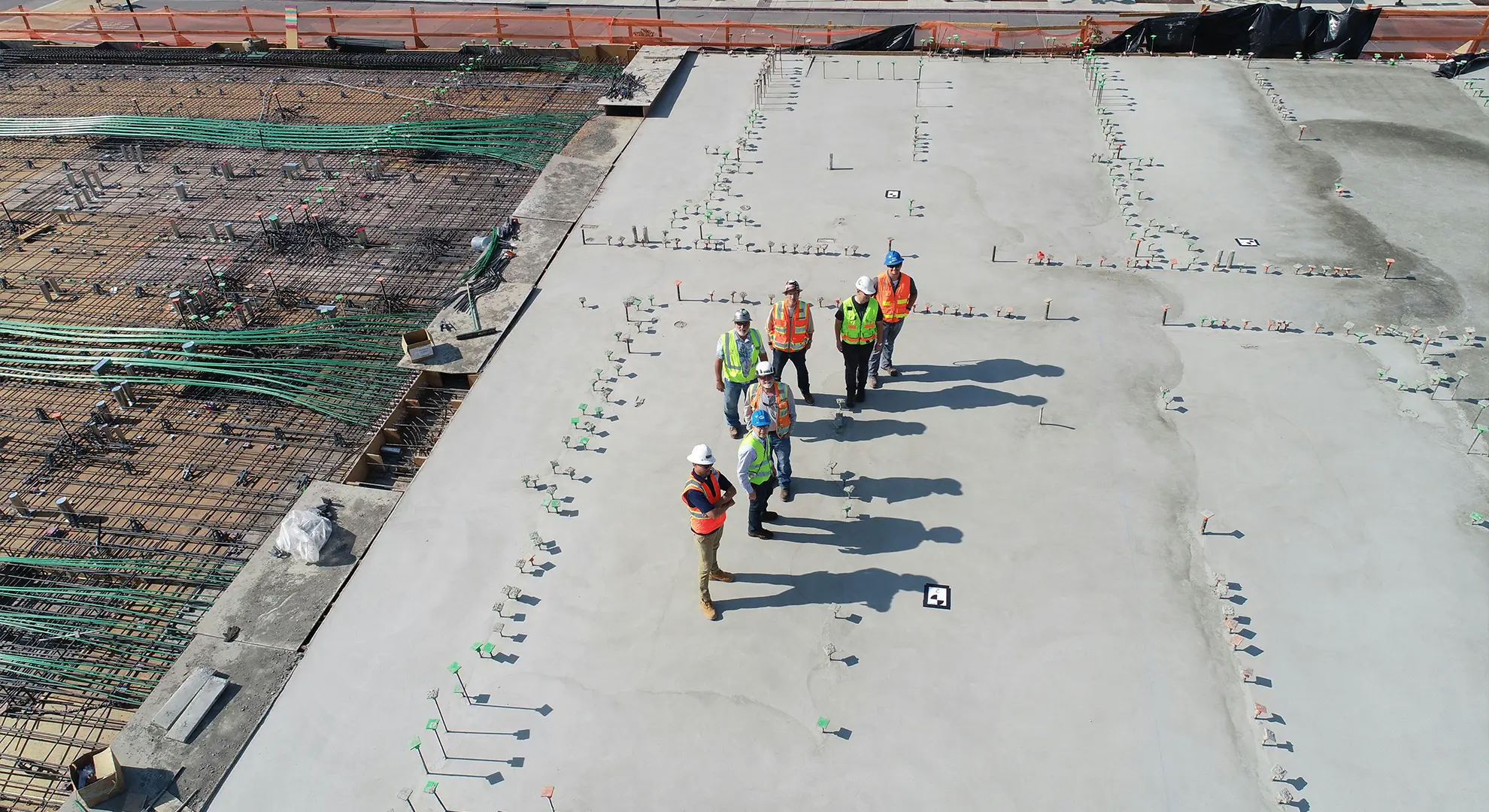 Construction workers in safety gear standing on a large concrete slab at a construction site
