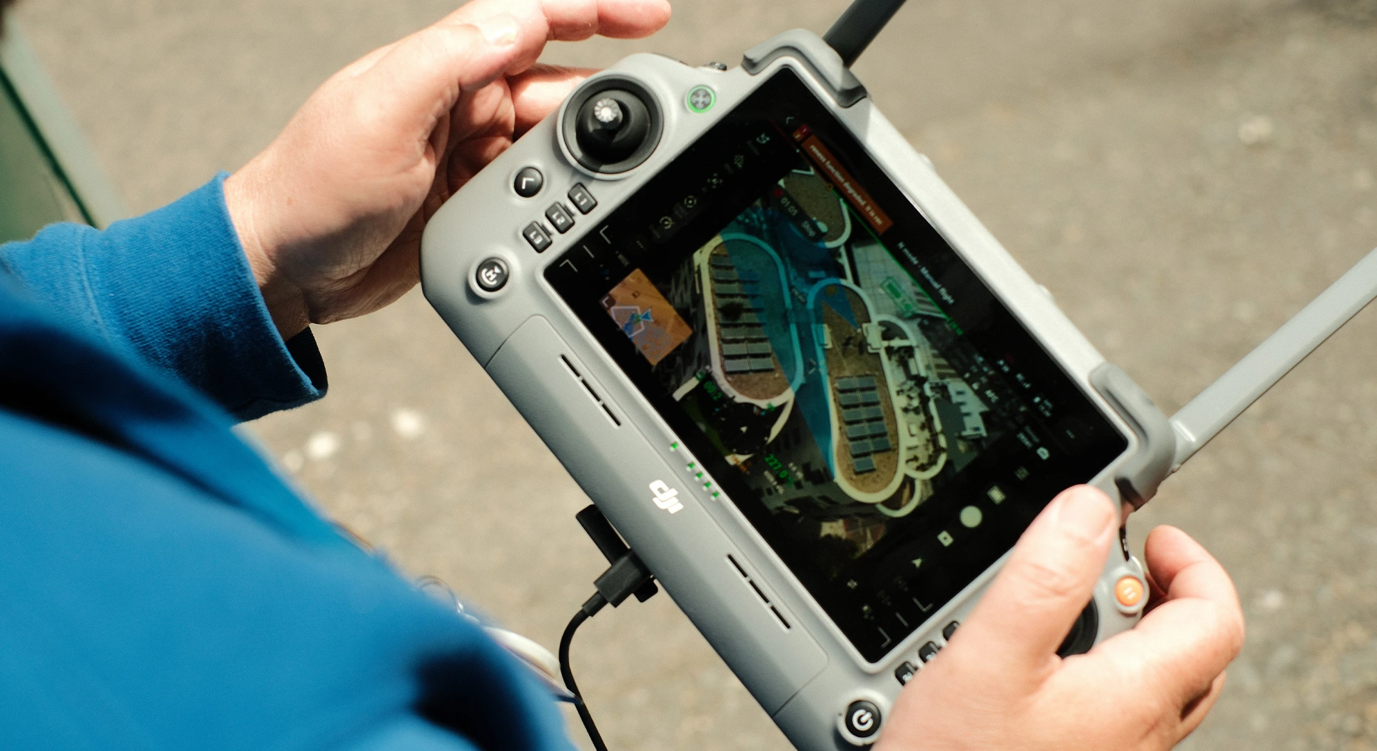 Close-up of hands holding a drone remote controller displaying a live aerial survey feed on the screen.